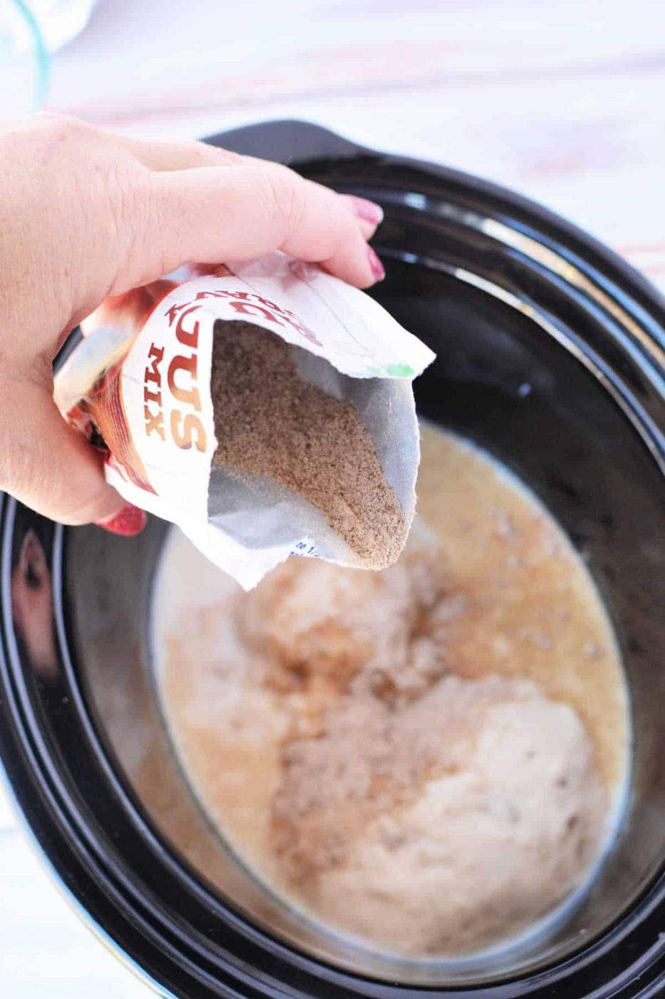 A hand pours dry biscuit mix from a packet into a slow cooker with liquid ingredients inside, preparing for a delicious Crockpot Salisbury Steak meal.
