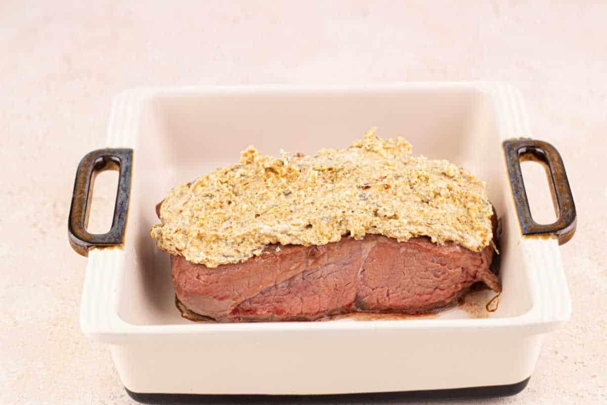 steak with a mustard and Parmesan crust in a white baking dish with handles.
