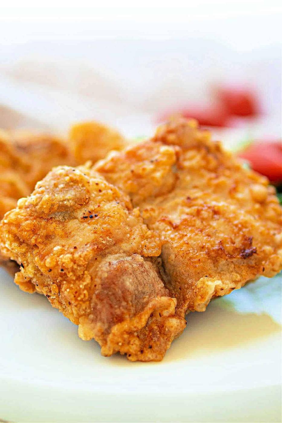 Close-up of a golden, crispy fried pork chops nestled on a white plate, reminiscent of the crunch youd find in perfectly deep-fried pork chops.