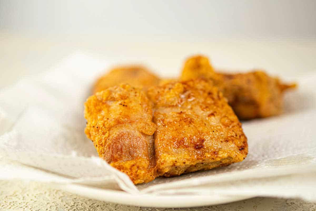 Close-up of crispy fried pork pieces, reminiscent of deep-fried pork chops, resting on a paper towel-lined plate.