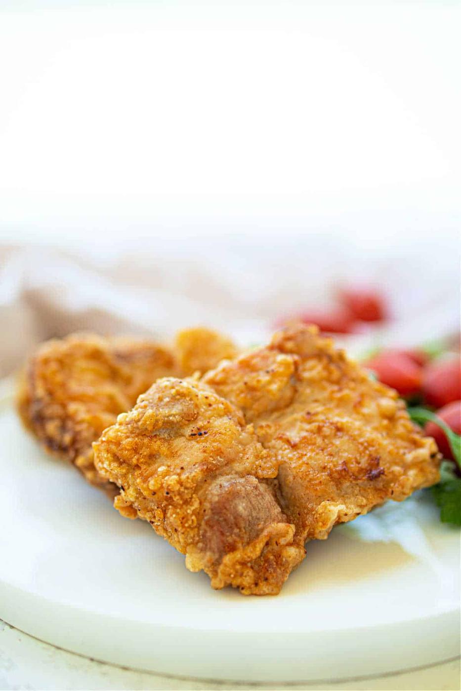 Crispy fried pork pieces share the plate with deep-fried pork chops, while cherry tomatoes brighten the background.