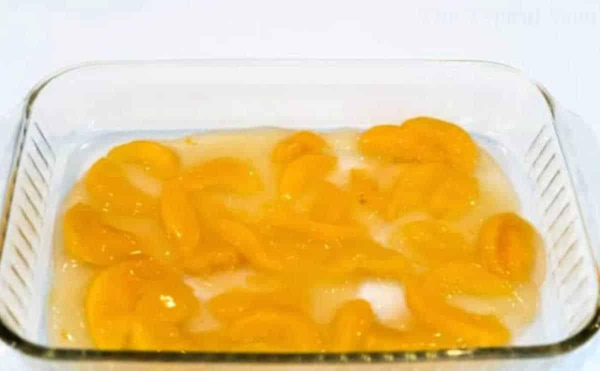 Glass dish with canned peach slices in syrup on a white surface, perfect for making an effortless dump peach cobbler.