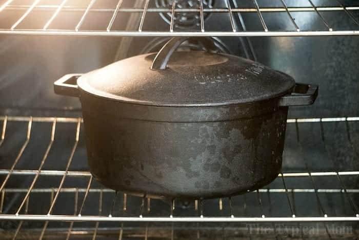A black cast iron pot, resembling a classic Dutch oven, sits on an oven rack with its lid firmly in place.