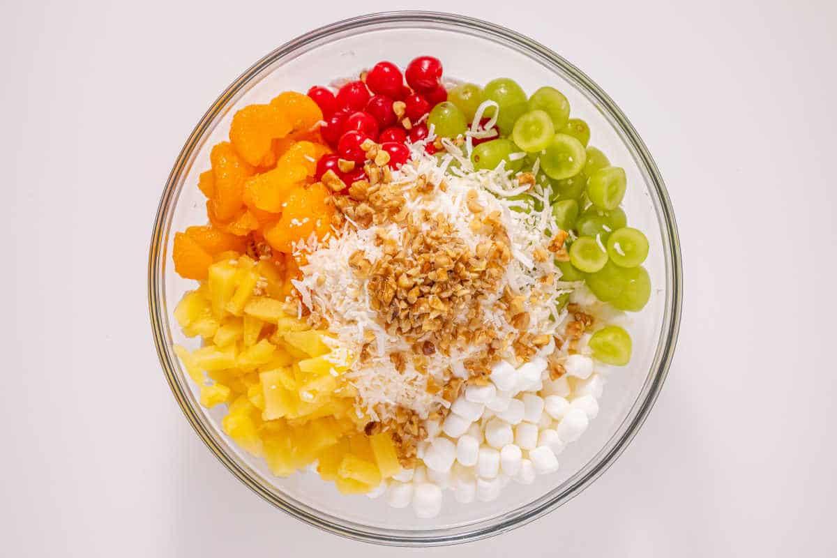 Glass bowl with grapes, pineapple, mandarin oranges, cherries, marshmallows, shredded coconut, and chopped nuts—an easy ambrosia recipe perfect for any occasion.