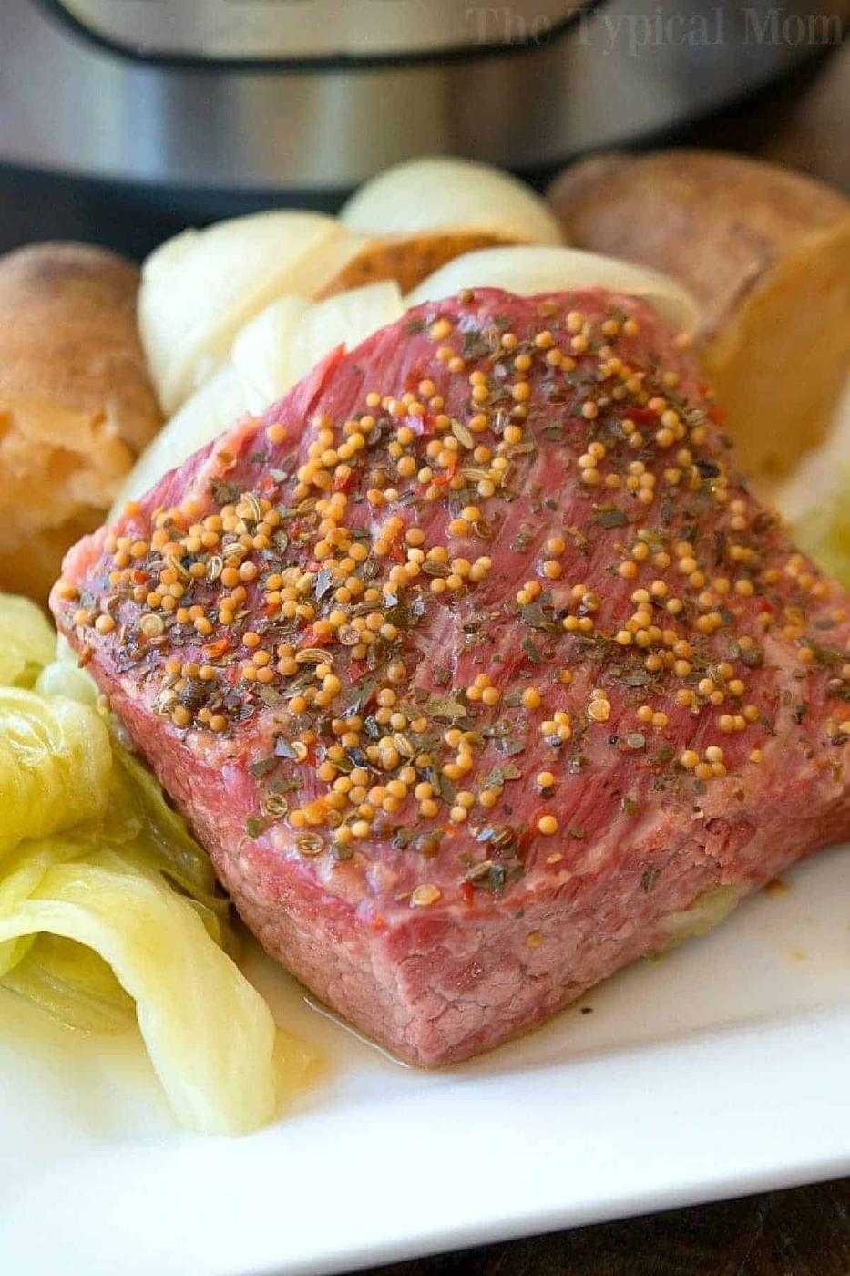 A slice of seasoned instant pot corned beef and cabbage, served with potatoes and onions on a white plate.