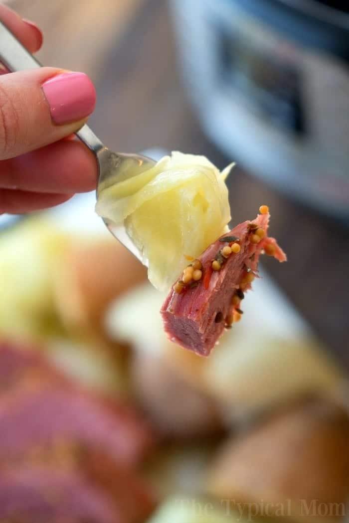 A fork with instant pot corned beef and cabbage held by a hand with pink nail polish.