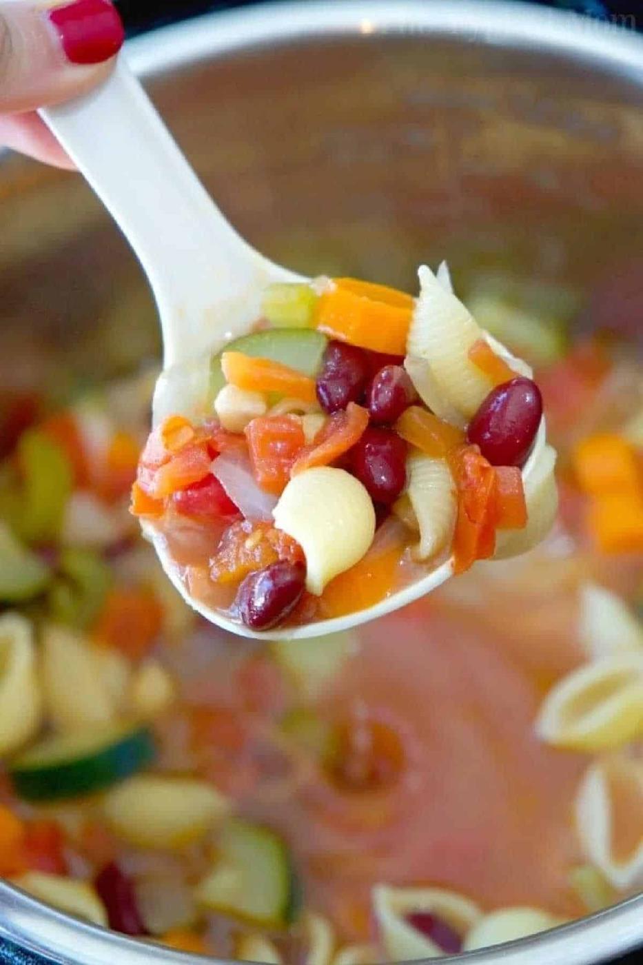 A spoonful of easy Instant Pot minestrone soup with pasta shells, beans, carrots, celery, and tomatoes hovers over a steaming pot.