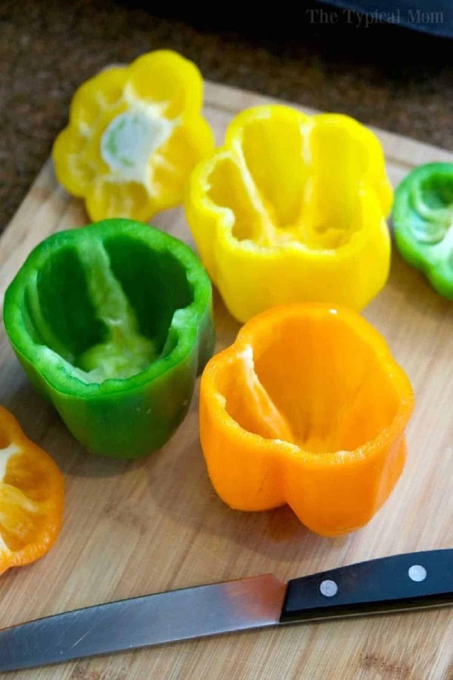 Hollowed green, yellow, and orange bell peppers on a cutting board with a knife, ready for easy Instant Pot stuffed peppers.