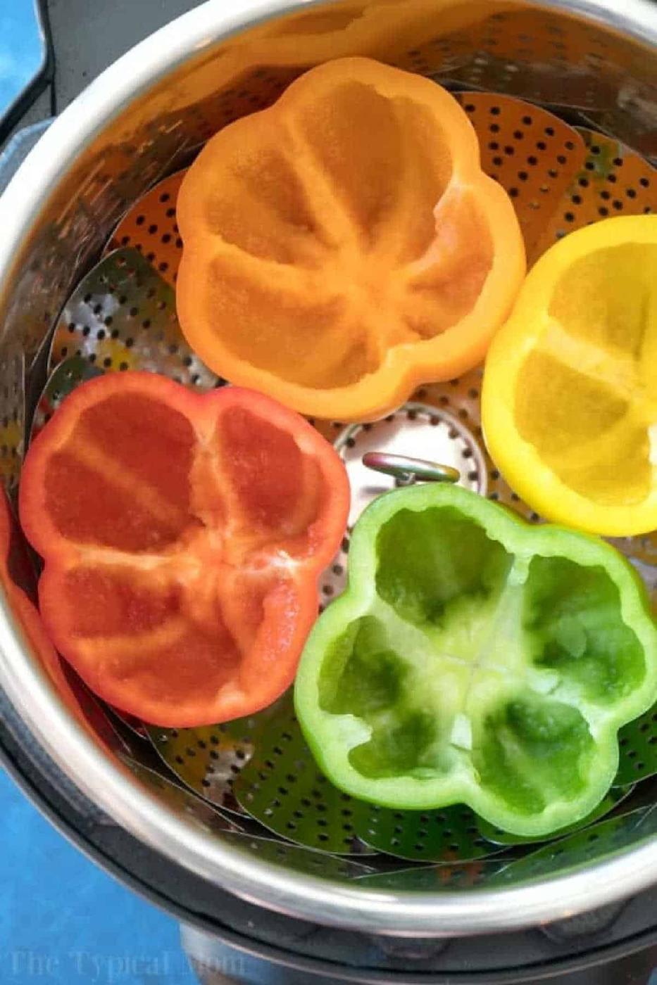 Four hollowed bell pepper halves—orange, yellow, red, and green—in a steamer basket, ready for easy Instant Pot stuffed peppers.