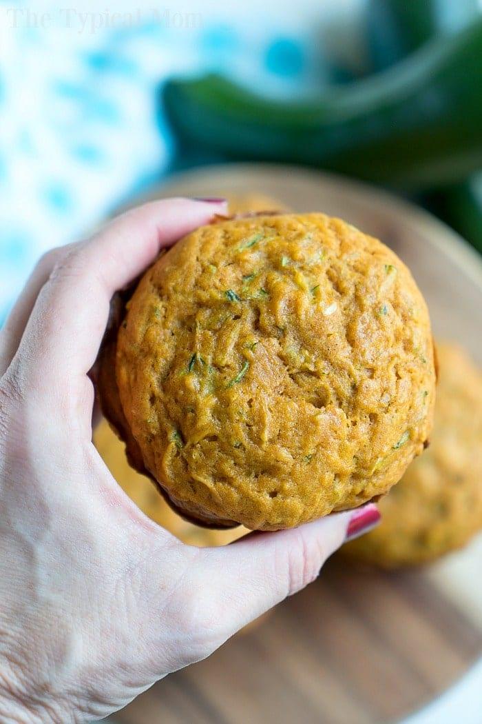 A hand holding a round, golden brown zucchini muffin with a soft texture—an easy muffin recipe perfect for delicious homemade treats.