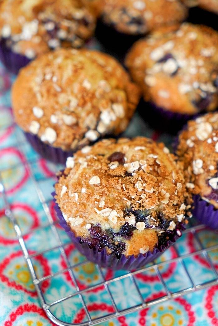 Blueberry muffins with oat crumble topping on a wire cooling rack, colorful patterned cloth underneath—an easy muffin recipe perfect for any occasion.