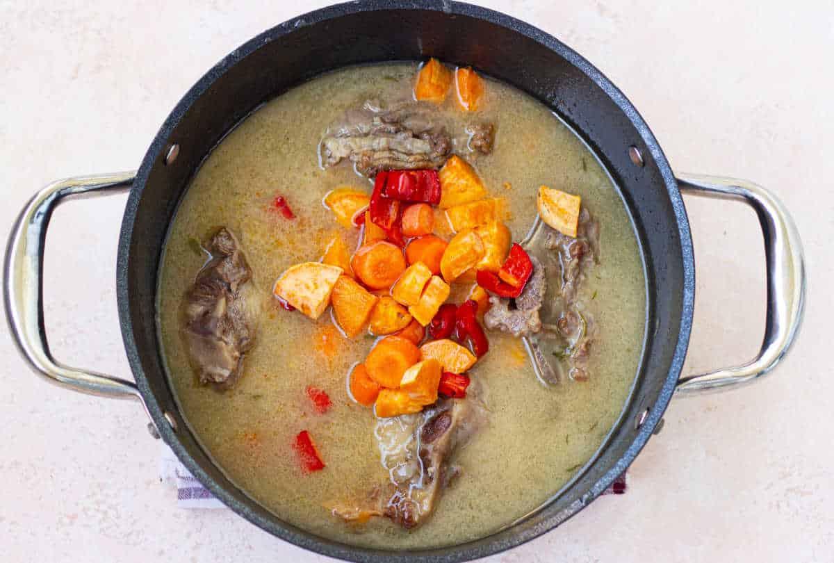 A pot of soup with tender beef ox tails, carrots, red peppers, and rich broth sits invitingly on a light background—a delightful hint for an easy oxtail recipe.