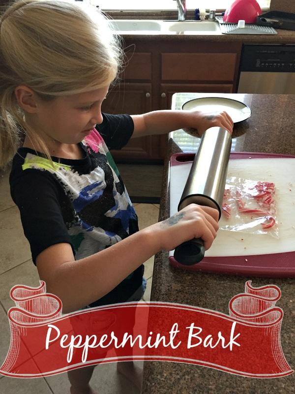 A young girl is using a rolling pin to crush peppermint candy pieces on a cutting board in a kitchen. The text "Microwave Peppermint Bark" is shown at the bottom of the image with a decorative ribbon banner.