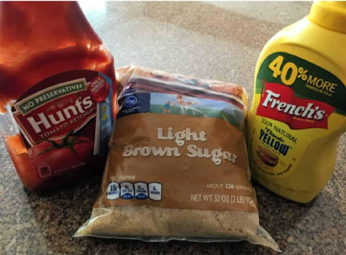 A bottle of Hunt’s ketchup, a bag of light brown sugar, and a bottle of French’s yellow mustard on a counter—perfect for an easy sloppy joe recipe with just 3 ingredients.