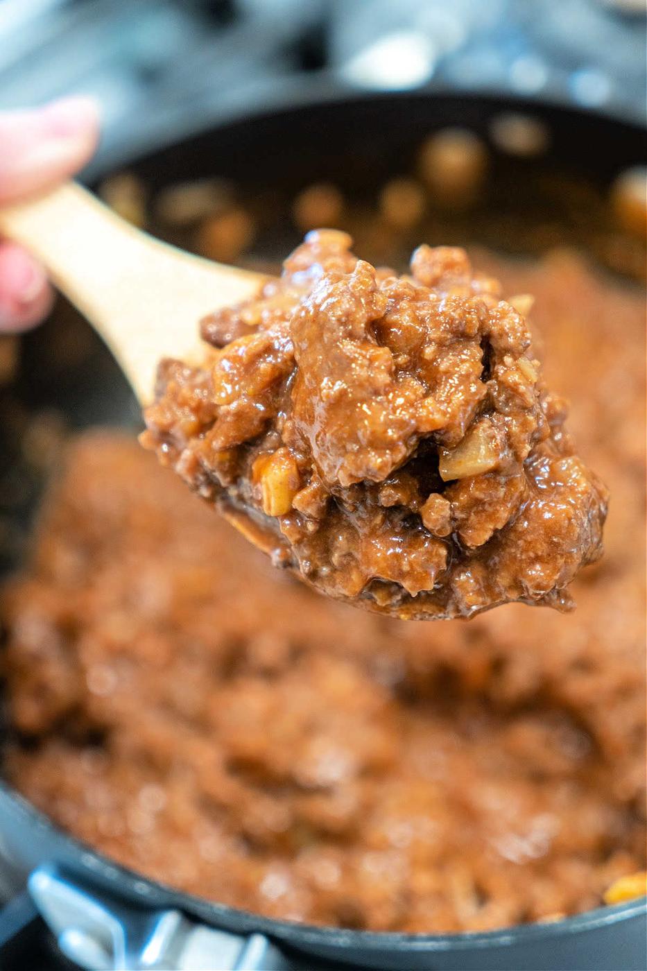 A wooden spoon holds a scoop of thick, chunky beef stew above a pot of the same stew—comfort food that’s almost as simple as an easy sloppy joe recipe with 3 ingredients.