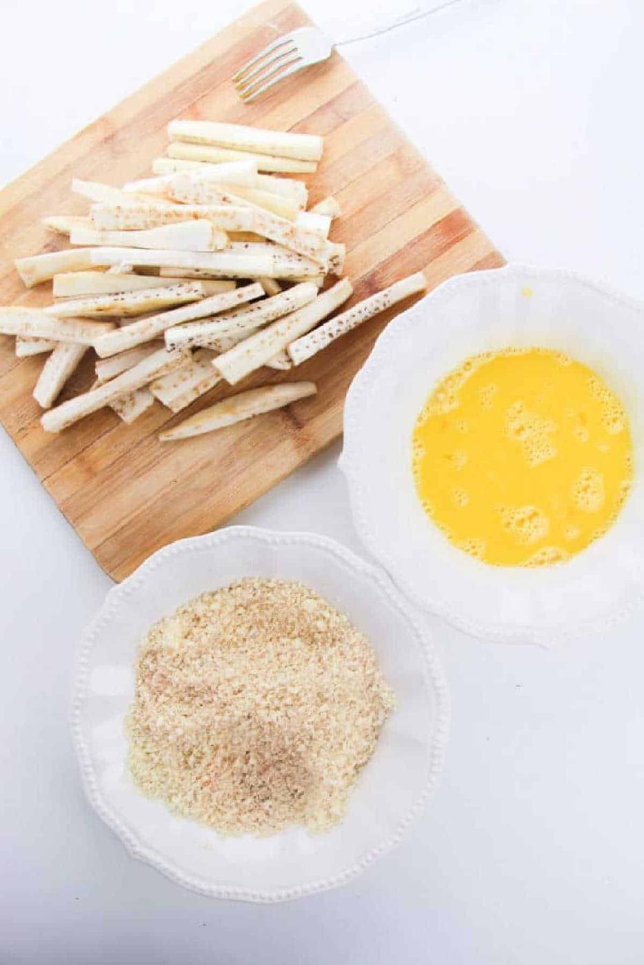 eggplant sticks on a cutting board, with bowls of beaten eggs and breadcrumbs next to them—perfect for making unique alternatives to Eggplant Fries.