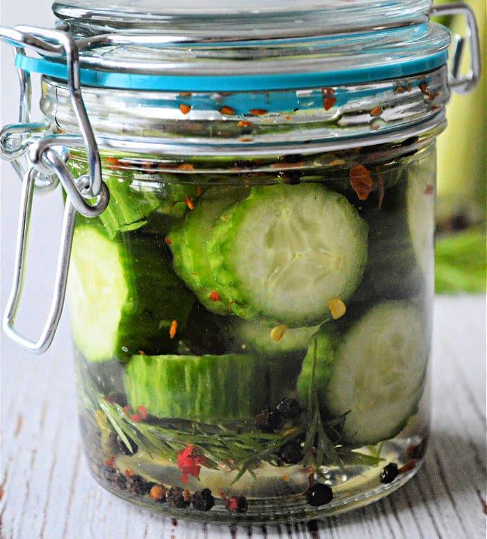 Jar of homemade sliced pickles with herbs and spices in brine, sealed with a clasp lid—perfect for those looking to master how to make pickles at home.