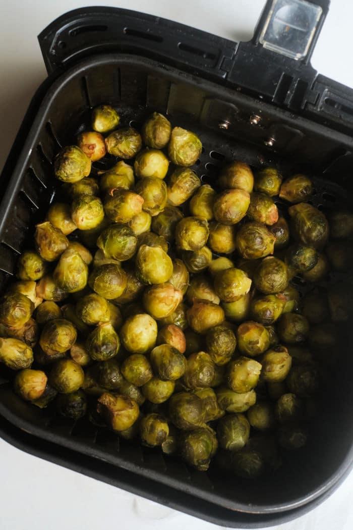 Air fryer basket filled with perfectly roasted frozen Brussels sprouts on a white background.