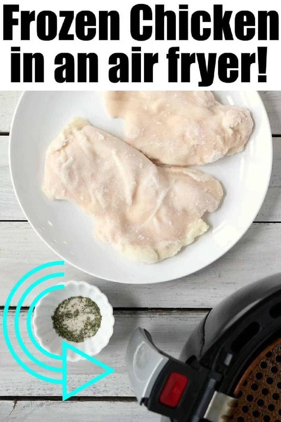 Frozen chicken breasts on a plate next to an air fryer and a small bowl of herbs on a white table, perfect for preparing frozen chicken breast in air fryer with fresh flavors.