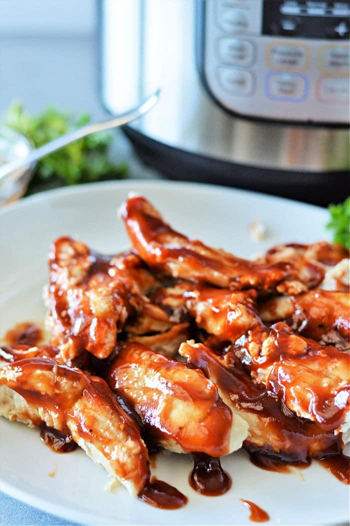 A plate of barbecue glazed chicken tenders cooked from frozen chicken tenders in the Instant Pot sits on a kitchen counter.