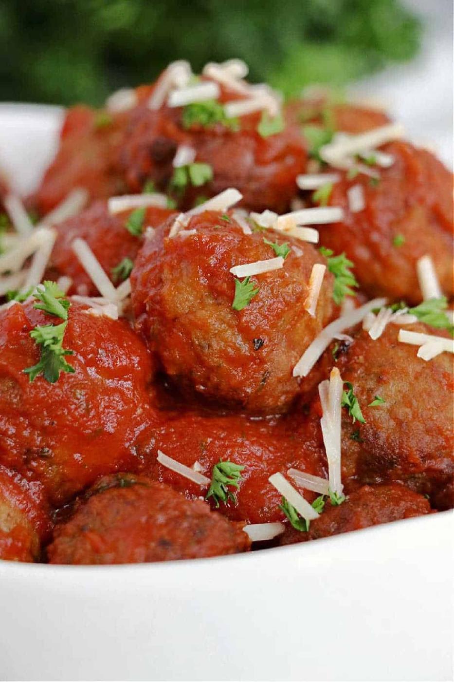 Frozen meatballs in air fryer are topped with marinara sauce, shredded cheese, and parsley, then served in a white bowl.