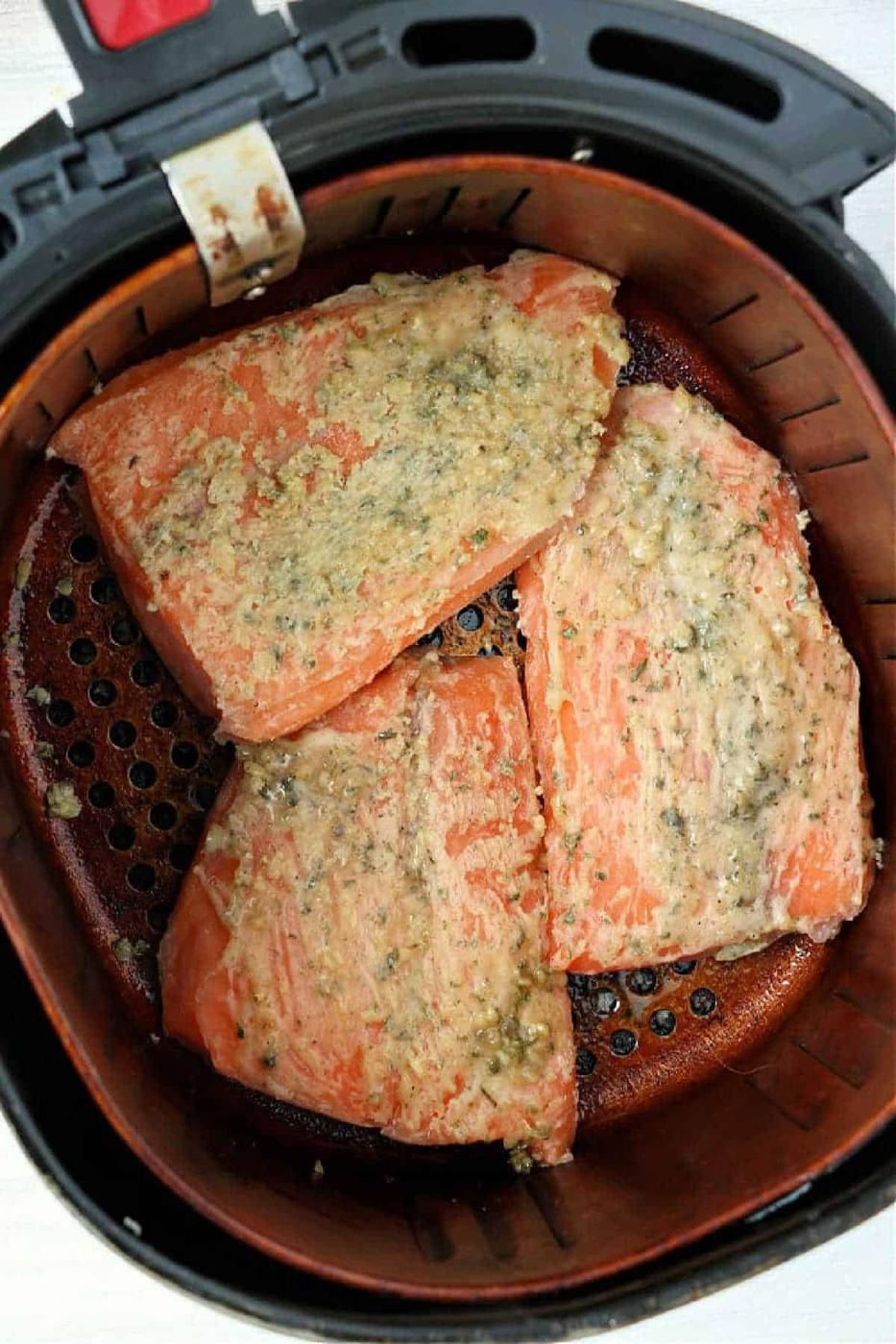 Three seasoned fillets of frozen salmon in air fryer basket, cooking to tender perfection.