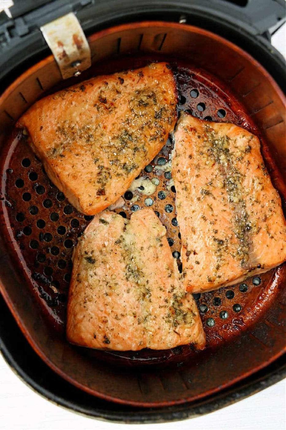 Three seasoned frozen salmon fillets cooked in an air fryer basket, showing a perfectly golden-brown exterior.