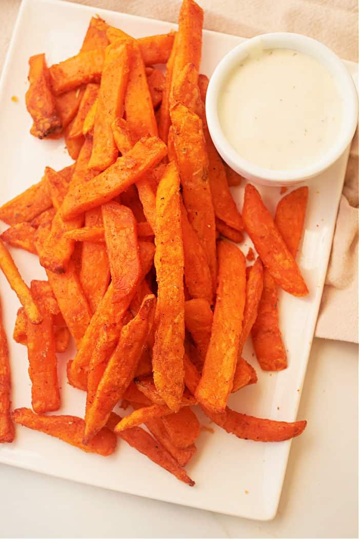 Frozen Sweet Potato Fries air fryer-cooked to perfection, served on a white plate with a small bowl of creamy dipping sauce.
