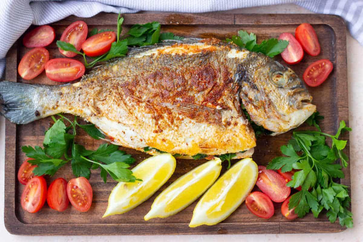 Enjoy a perfectly cooked whole fish served on a wooden board, garnished with lemon wedges, cherry tomatoes, and parsley—a delightful alternative to frying a whole fish.