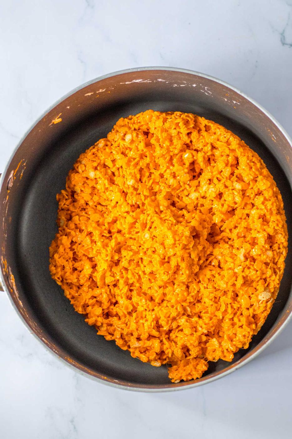 A pan filled with bright orange marshmallow cereal trats is positioned on a marble surface, reminiscent of Halloween Rice Krispie Treats.