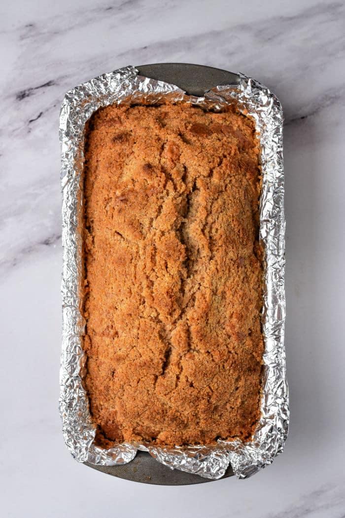 A freshly baked healthy coffee cake loaf rests in a foil-lined pan on a marble surface