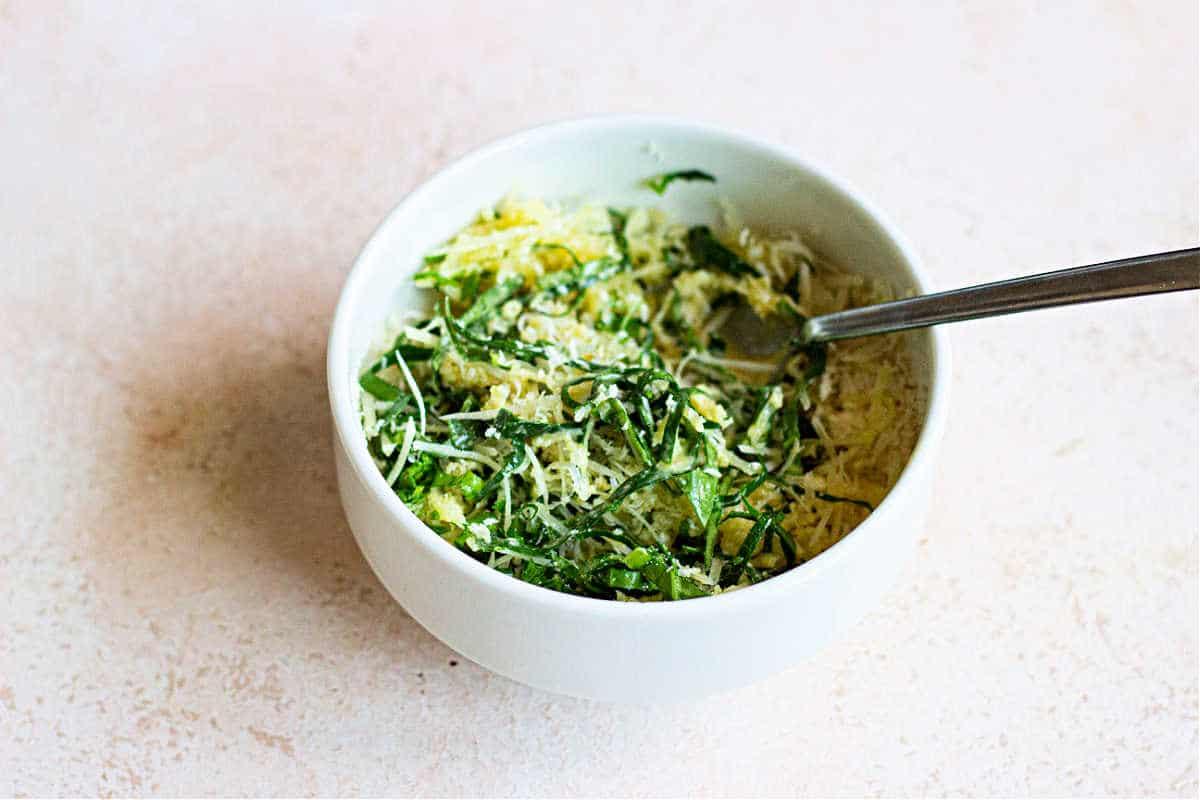 A bowl of vibrant greens, topped with slices of herbed crusted chicken, and a fork rests invitingly on the light surface.