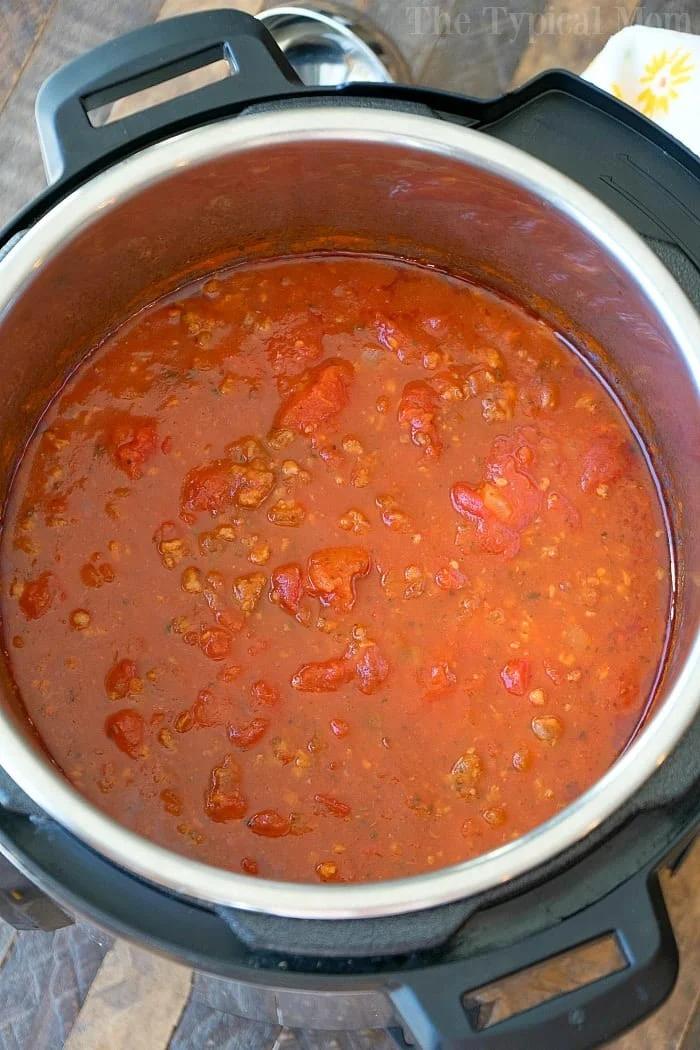 An open Instant Pot reveals a hearty sauce simmering with tomatoes and ground meat, reminiscent of a robust spaghetti sauce.