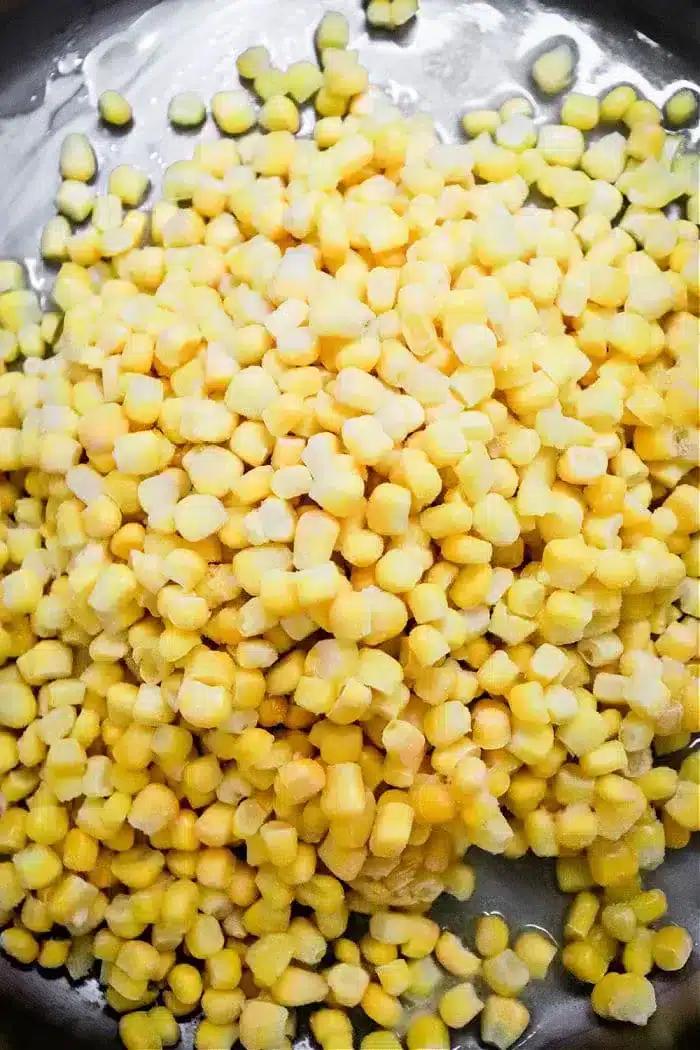 A close-up view of a heap of fresh or possibly frozen yellow and white corn kernels, piled on a dark surface, promises the delicious potential of Honey Butter Skillet Corn.