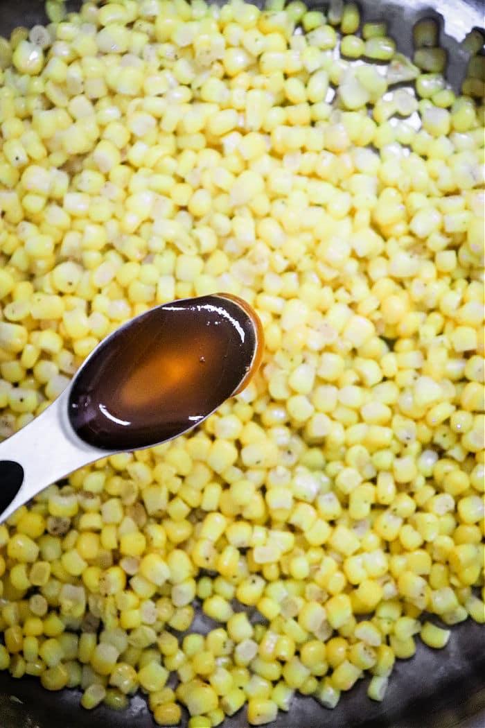 A spoon with honey hovers above a skillet of Honey Butter Skillet Corn, perfectly sautéed for a deliciously sweet and savory dish.