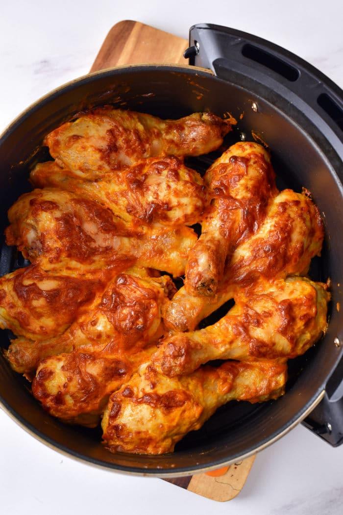 Baked chicken drumsticks coated in sauce rest in a black baking dish on a wooden board, making you wonder how long to boil chicken legs before achieving this savory perfection.