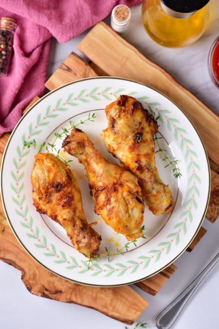 A plate of chicken drumsticks, perfectly timed after learning how long to boil chicken legs for tender flavor, is garnished with herbs. Set on a rustic wooden board against a pink cloth backdrop, it’s a feast for both the eyes and the palate.