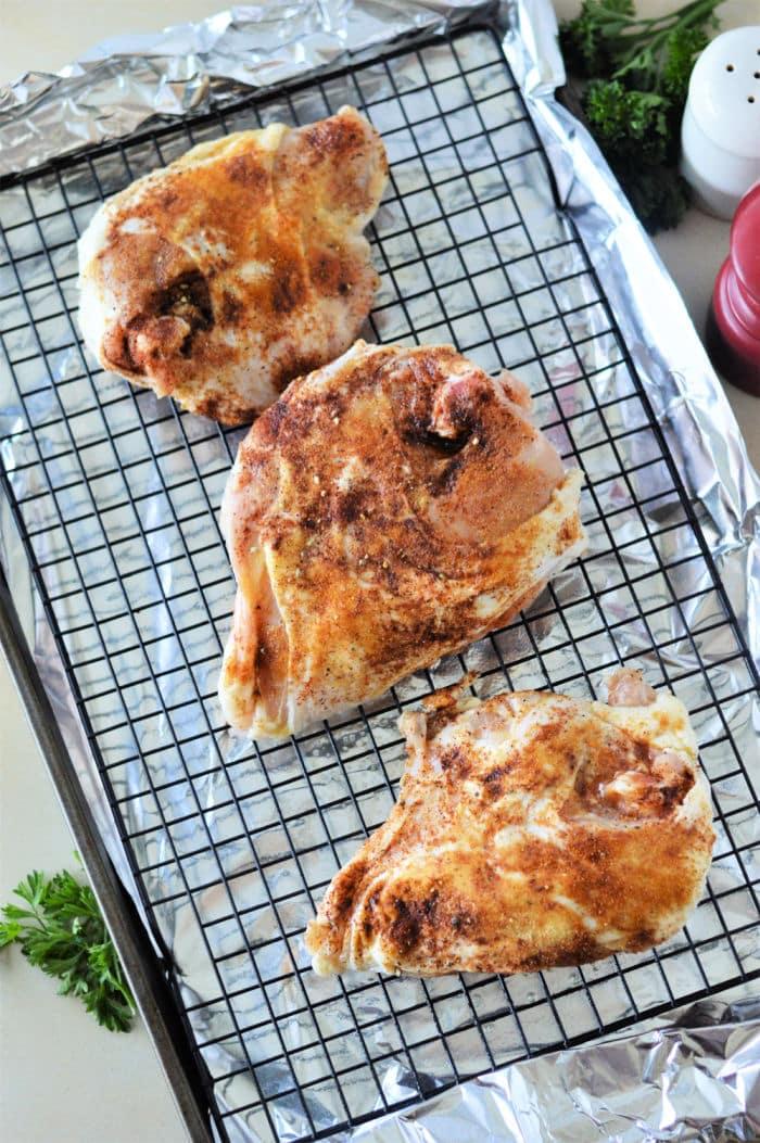 Three seasoned chicken breast on a wire rack over foil, ready for baking at 350°F—a perfect setup reminiscent of how you’d prepare chicken breast to achieve tender results.