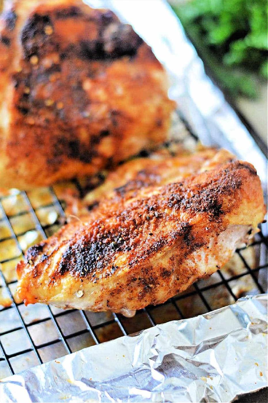 roasted chicken breast with seasoning rests on a wire rack over foil, perfect for even cooking. Curious about oven time? Bake at 350°F for a juicy finish.