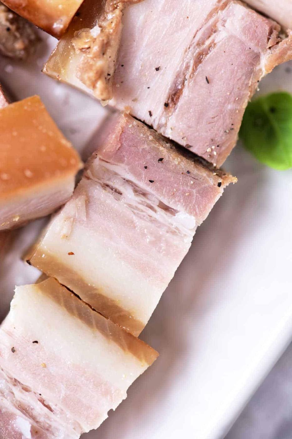 Close-up of sliced pork belly on a plate, showcasing layers of fat and meat, a delicious result reminiscent of the techniques used in how to confit pork.