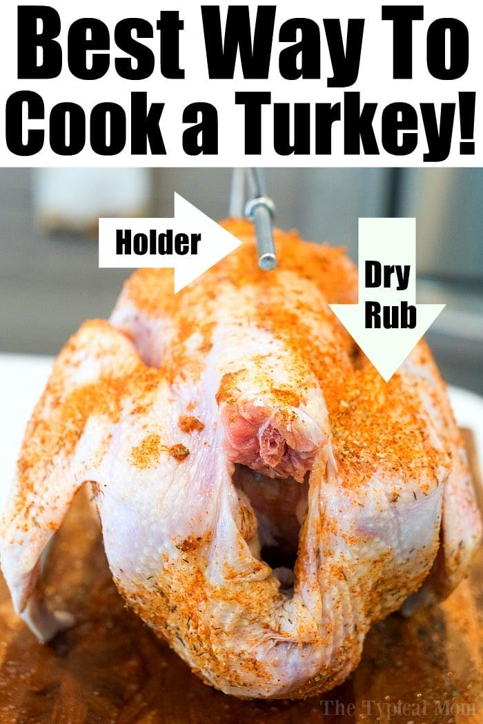 Raw turkey seasoned with a dry rub sits on a holder, ready for cooking. The image features text indicating "Best Way To Cook a Moist Turkey!" with arrows pointing to the holder and dry rub.