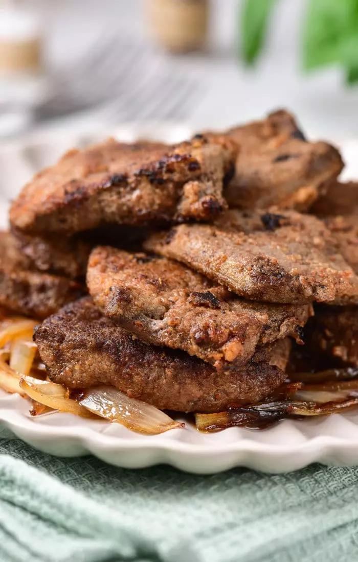 A plate of fried liver slices stacked on top of caramelized onions, demonstrating how to cook beef liver perfectly.