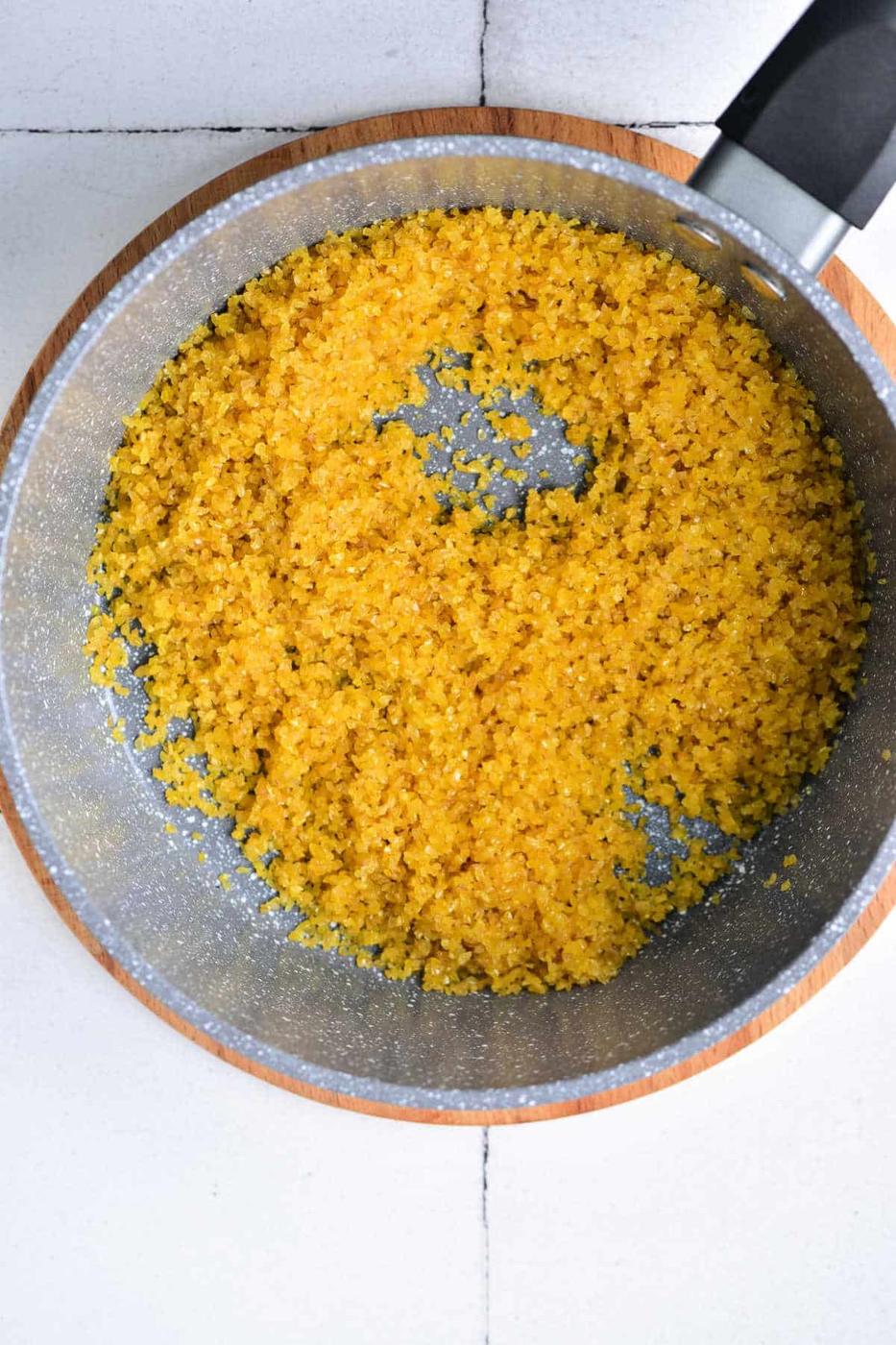 A pot with cooked yellow bulgar wheat rests on a wooden board, reminiscent of how to cook bulgur wheat in its simplicity and flavor.