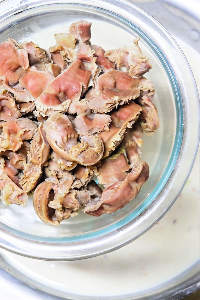A glass bowl filled with cooked chicken gizzards, seen from above—perfect for learning how to make gravy from chicken drippings.