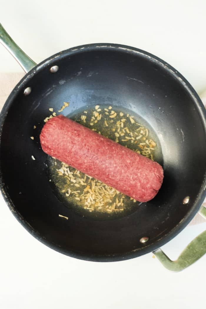 A black frying pan filled with raw frozen ground beef and chopped onions sizzles, reminiscent of a guide on how to cook frozen ground beef.