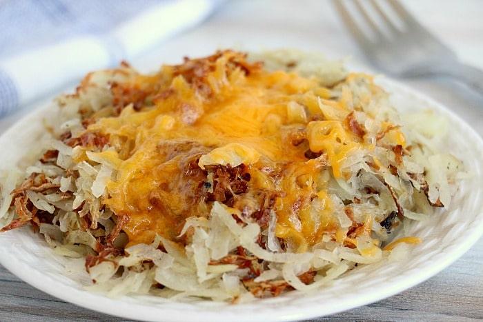 A plate of cheesy air fryer hash browns rests invitingly on a white table.