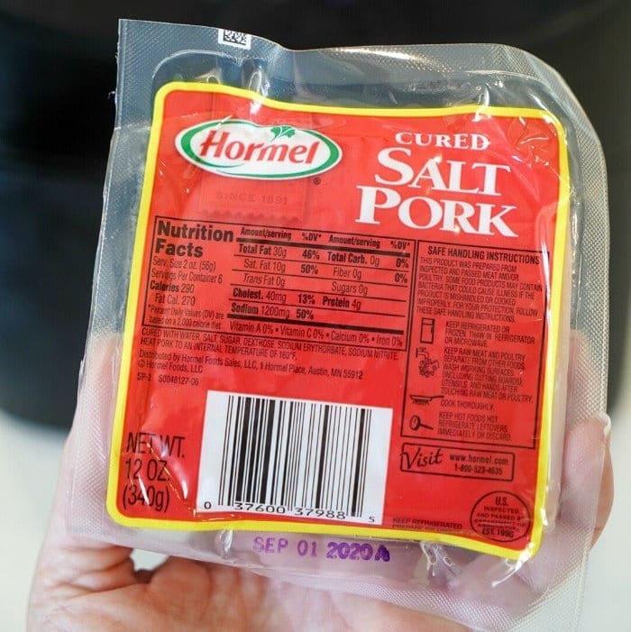 A hand holds a sealed package of Hormel cured salt pork with a nutrition label and a best by date of Sep 01 2023, perfect for those learning how to cook pork belly in the oven.