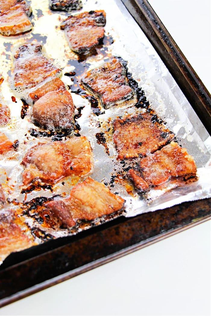 Crispy bacon pieces on a foil-lined baking sheet, some edges charred and glistening with grease—this is a perfect example of how to cook pork belly in the oven for that irresistible crunch.