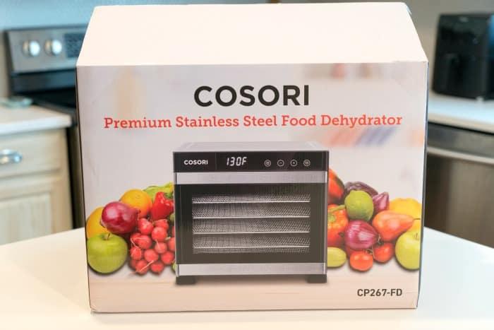 Box for a COSORI stainless steel food dehydrator, featuring images of fruits and vegetables on the front and tips on how to dehydrate apples for healthy homemade snacks.