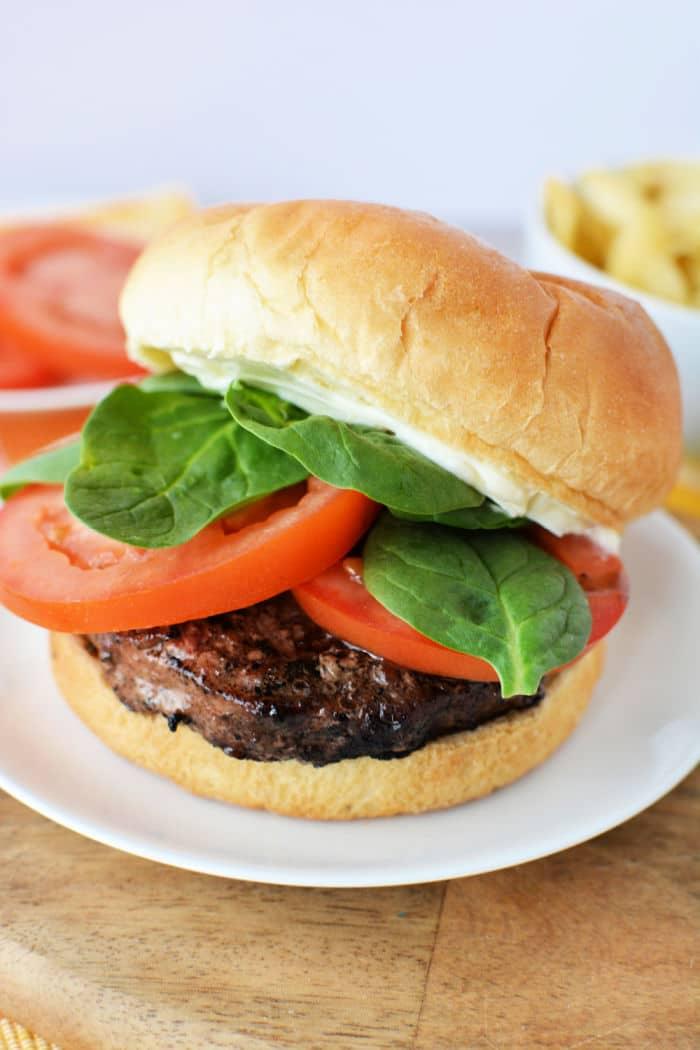 A hamburger with lettuce, tomato, and mayonnaise on a bun, served on a white plate—perfect inspiration if you're learning how to grill frozen burgers to juicy perfection.